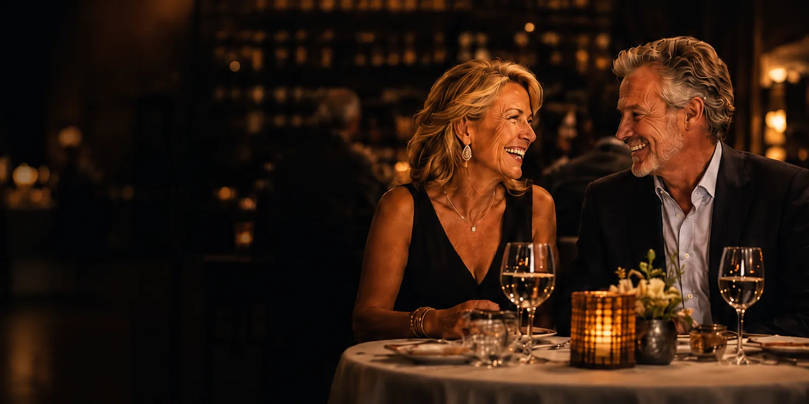 A couple laughing together over wine at a candlelit restaurant table.